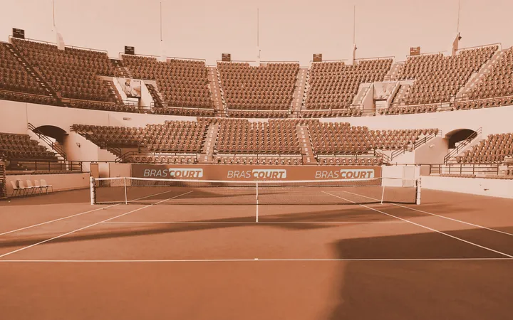 Banner do site da Brascourt: quadra de tênis num estádio vazio, em tom terroso, com a marca nas placas atrás da rede
