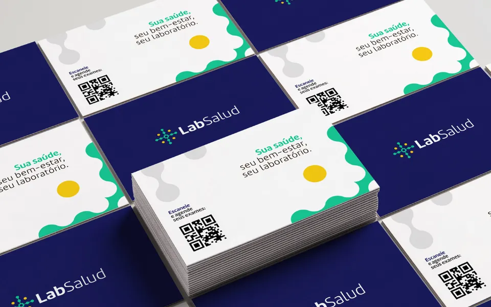 Cartões de visita da LabSalud espalhados sobre a mesa, alternando o verso azul-marinho com o logotipo e a frente branca com a frase Sua saúde, seu bem-estar, seu laboratório